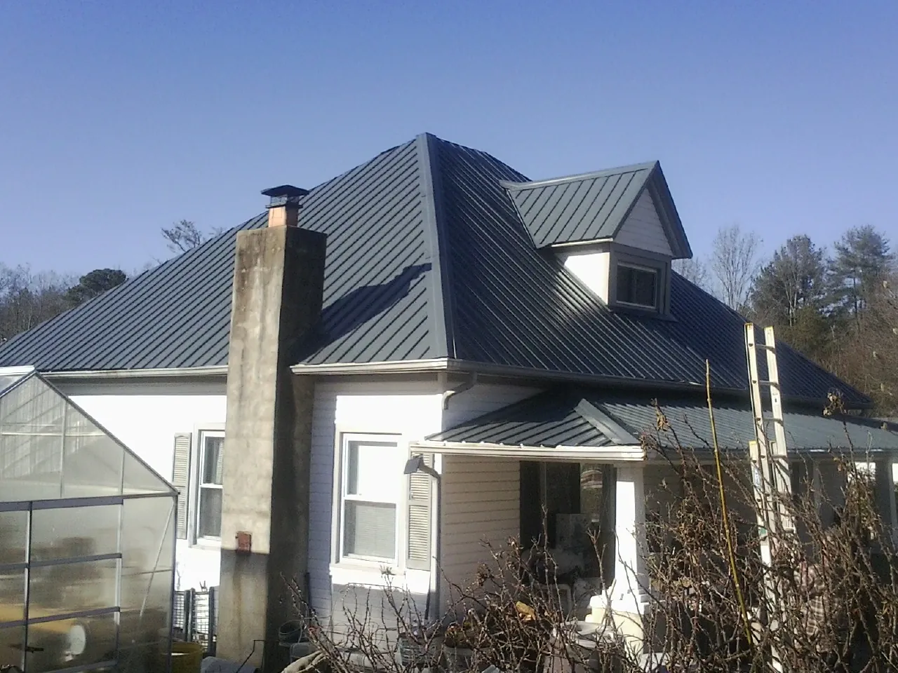 Dark blue standing seam metal roof on a white farmhouse with dormer — Slate & Tile Roof Repair by Roofing Brothers in Guinda