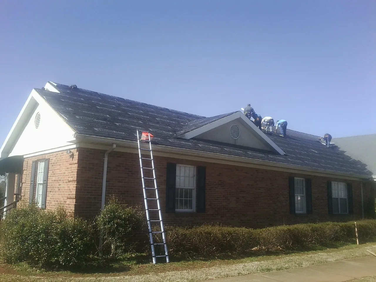 Crew tearing shingles off a brick ranch roof with a ladder set — Metal Roof Repair work by our crew in Guinda