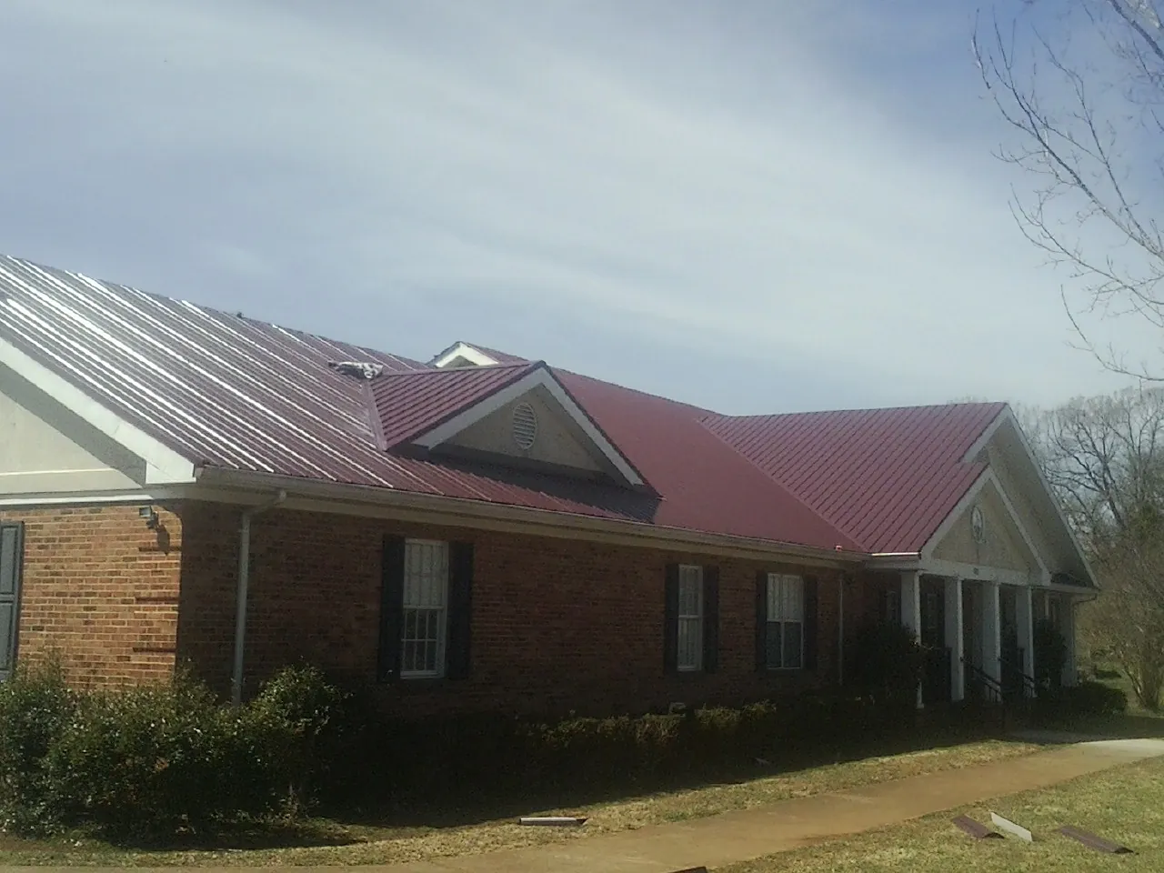 Red metal roof with gabled entries on a long brick building, from a Hail Damage Roof Repair job in Guinda