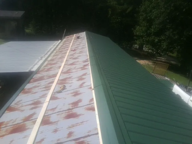 Old rusted panels beside newly installed green metal roofing — Wind Damage Roof Repair by Roofing Brothers in Guinda