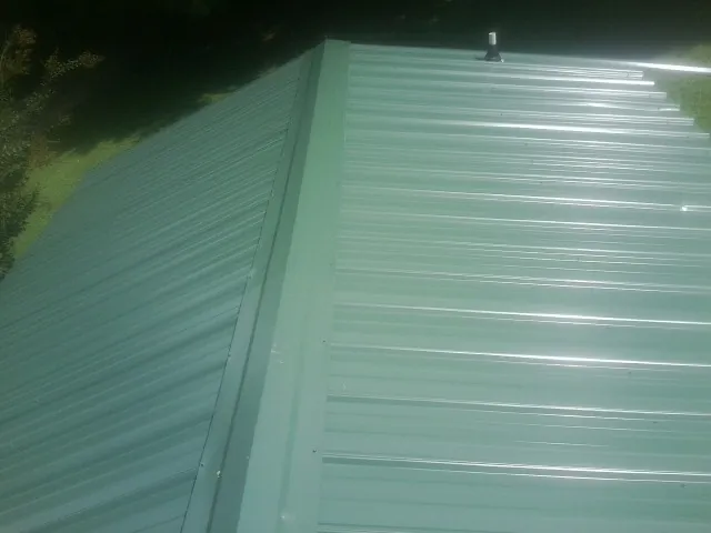 New green metal panels meeting at the ridge of a roof — Flat Roof Repair work by our crew in Guinda