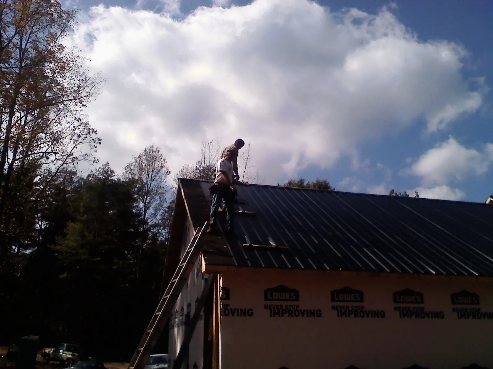 Roofer fastening dark metal panels high against a cloudy sky, from a Roof Inspection job in Guinda
