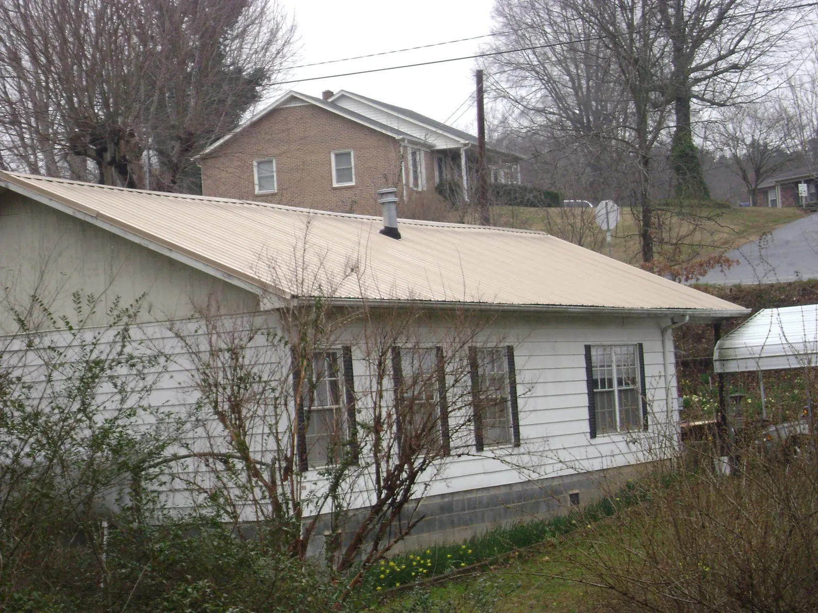 Tan metal roof on a white sided house set into a hillside — Commercial Roofing by Roofing Brothers in Guinda